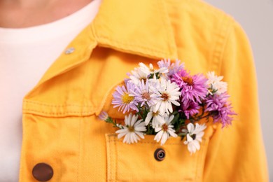 Photo of Woman with beautiful tender flowers in jacket's pocket on light background, closeup
