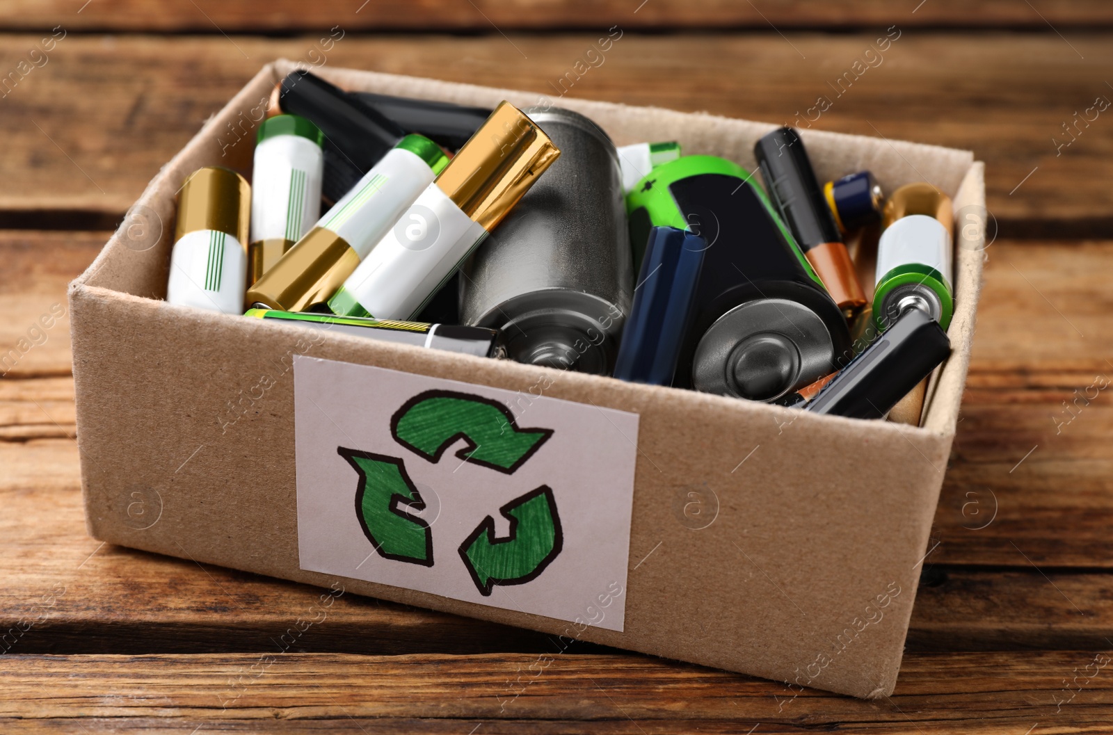 Image of Used batteries in cardboard box with recycling symbol on wooden table, closeup