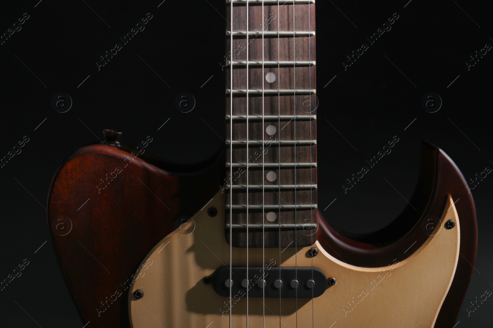 Photo of Modern electric guitar in darkness, closeup view