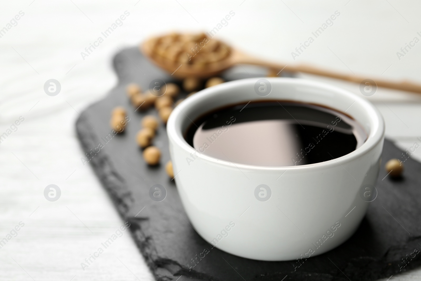 Photo of Slate board with bowl of soy sauce on wooden table. Space for text