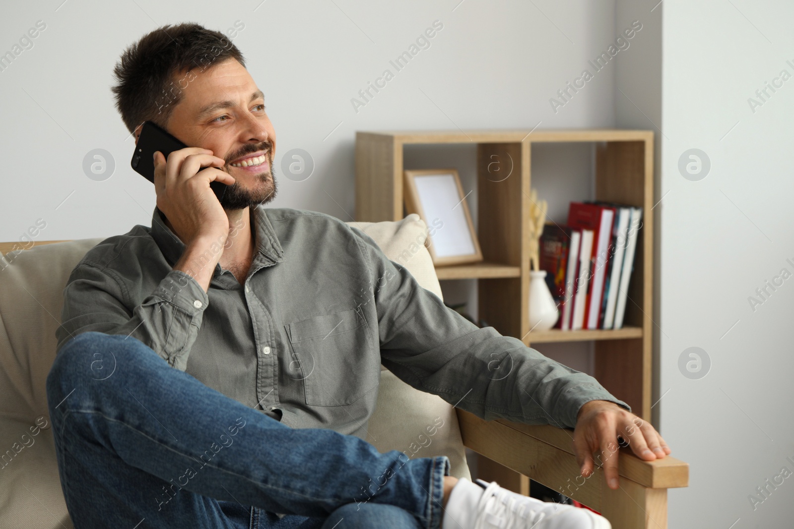 Photo of Happy man talking on smartphone at home