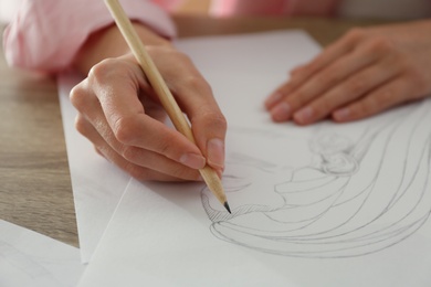 Photo of Woman drawing girl's portrait with pencil on sheet of paper at wooden table, closeup