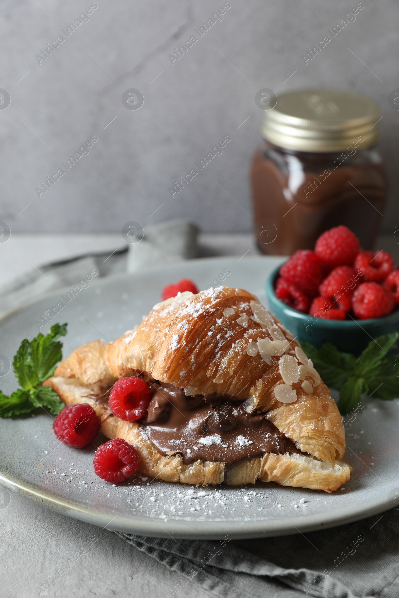 Photo of Delicious croissant with chocolate and raspberries on grey table