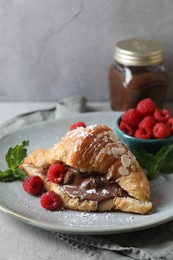 Delicious croissant with chocolate and raspberries on grey table