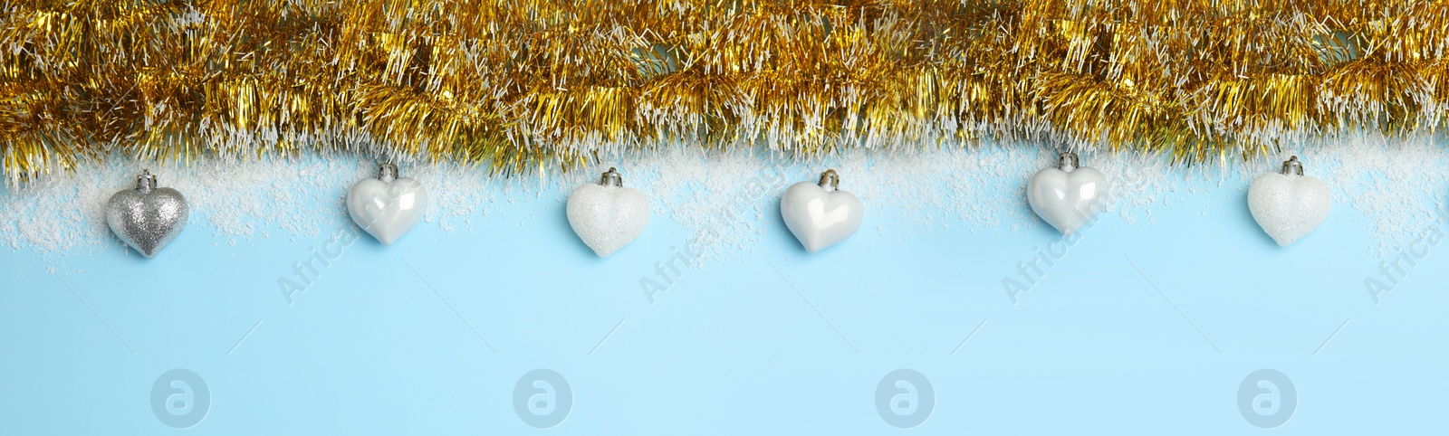 Image of Shiny golden tinsel, Christmas baubles and snow on light blue background, flat lay. Banner design