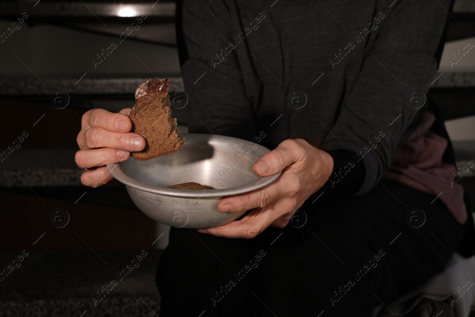 Photo of Poor mature woman with bowl and bread on stairs, closeup