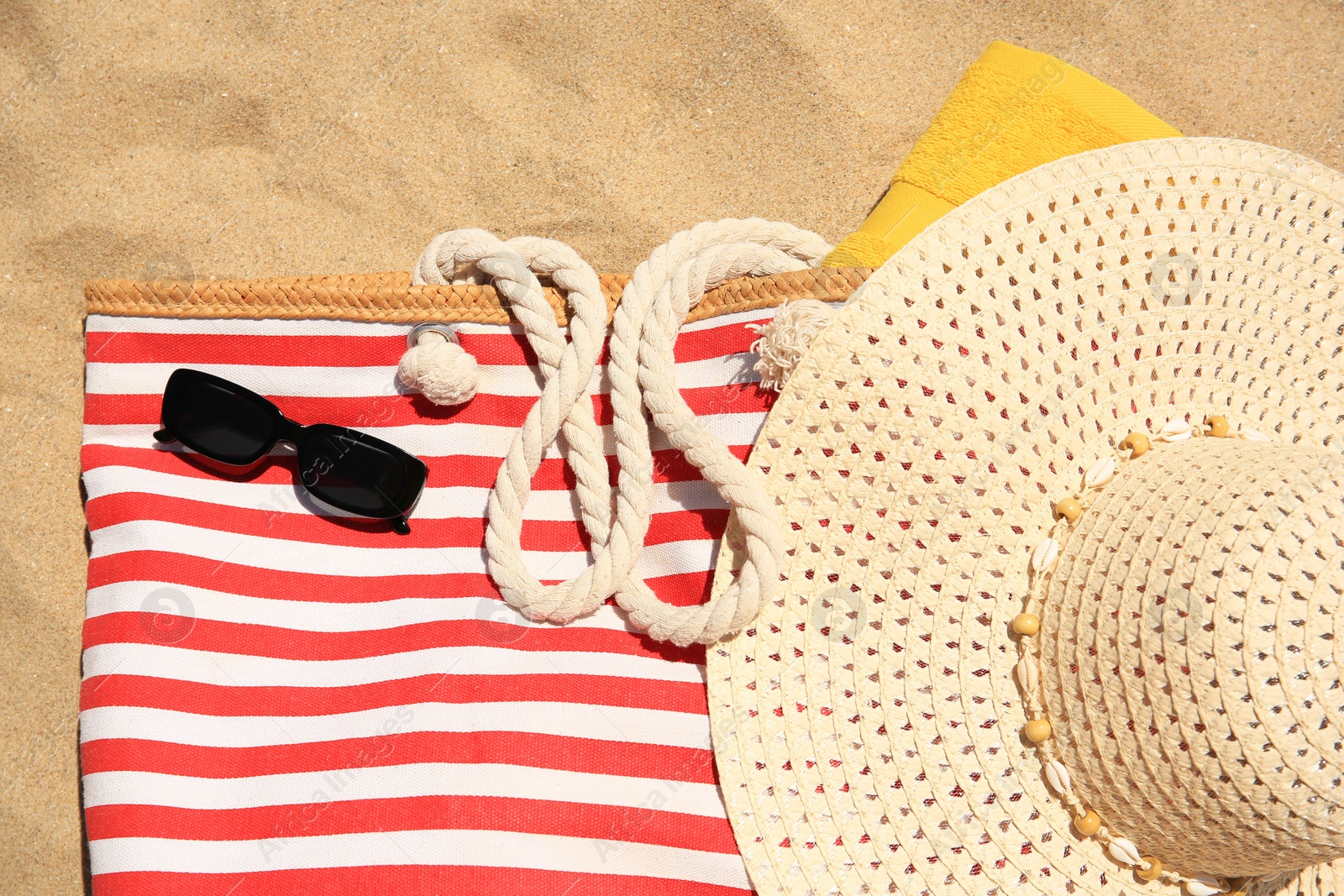Photo of Striped beach bag, sunglasses, towel and hat on sand, flat lay