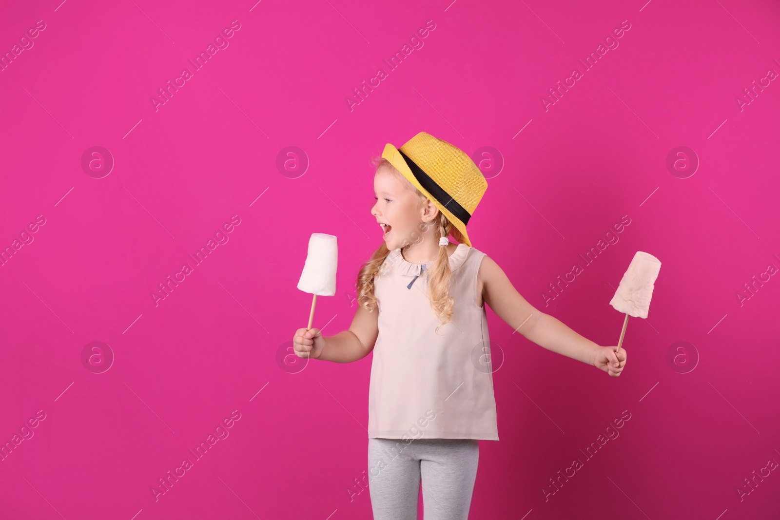 Photo of Cute little girl with cotton candies on color background