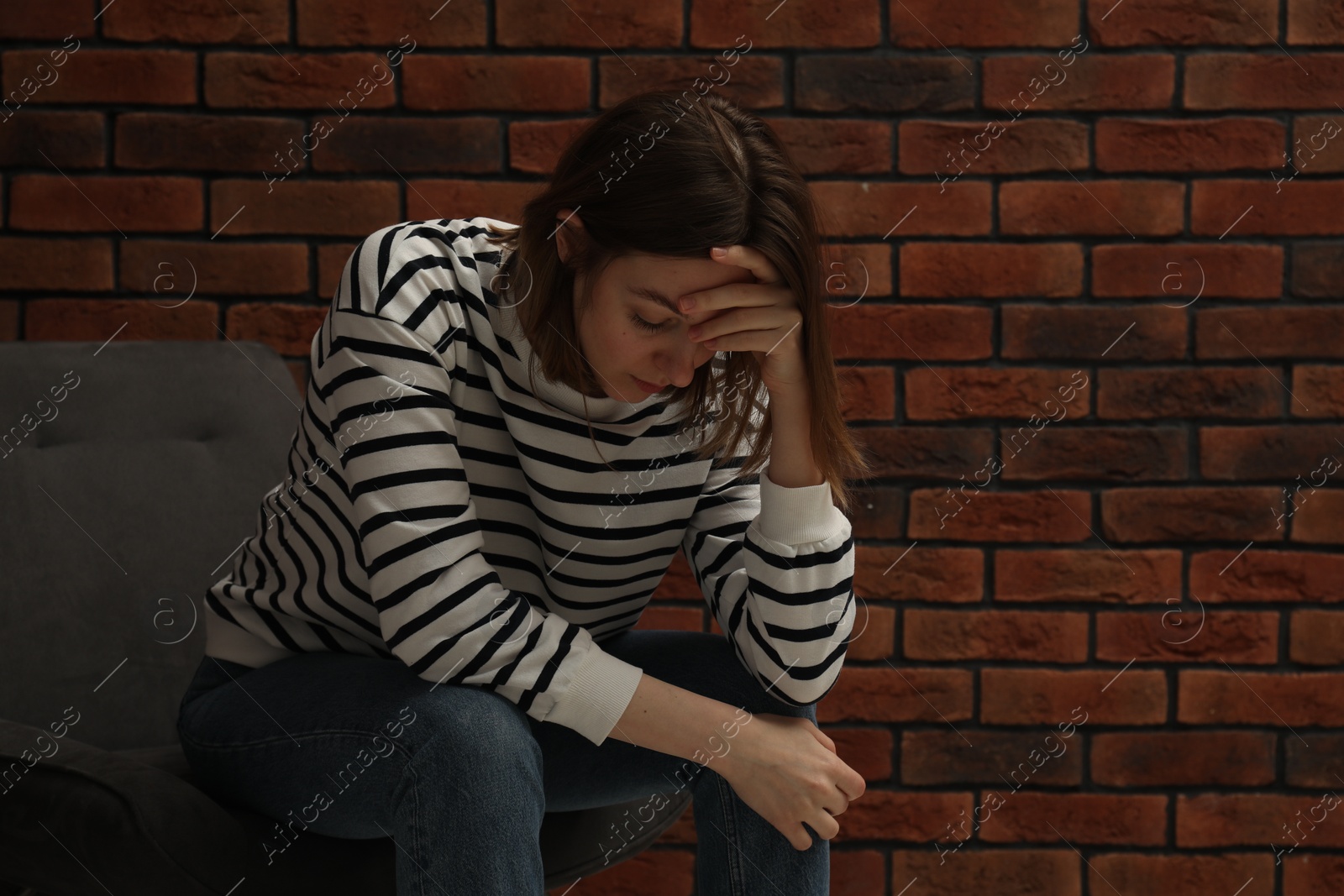 Photo of Sad young woman sitting on chair near brick wall, space for text