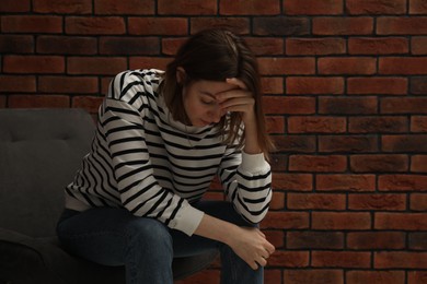 Photo of Sad young woman sitting on chair near brick wall, space for text