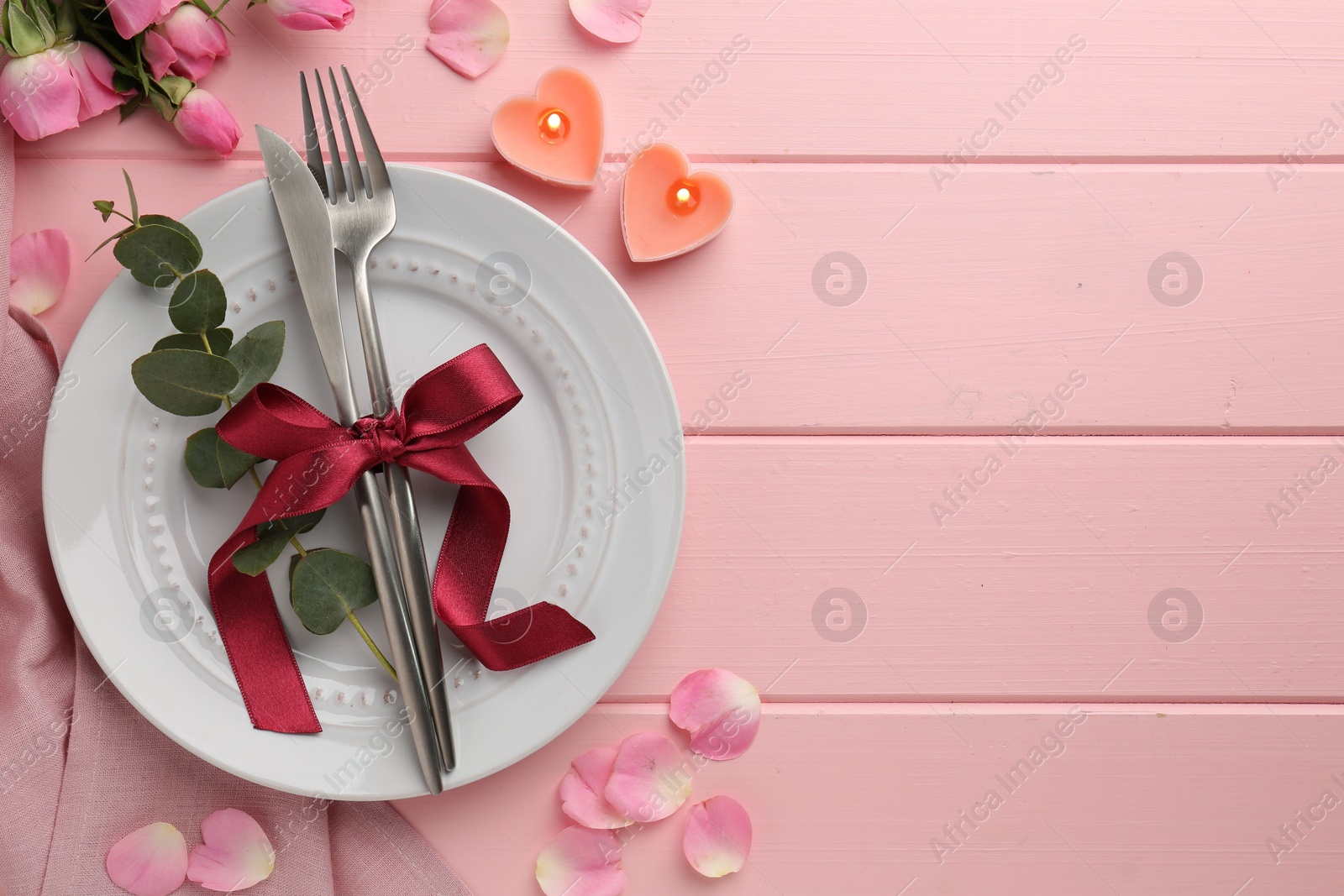 Photo of Place setting with heart shaped candles and bouquet of roses for romantic dinner on pink wooden table, flat lay. Space for text