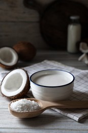 Photo of Bowl of delicious coconut milk, spoon with flakes and nuts on white wooden table, space for text