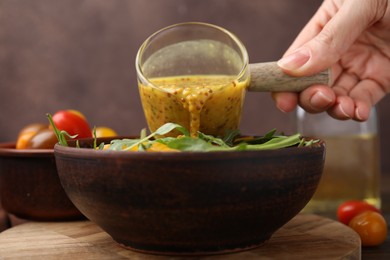 Woman pouring tasty vinegar based sauce (Vinaigrette) into bowl with salad at wooden table, closeup