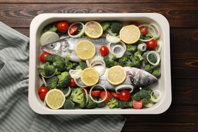 Raw fish with vegetables and lemon in baking dish on wooden table, top view