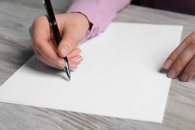 Photo of Woman writing on sheet of paper with pen at wooden table, closeup