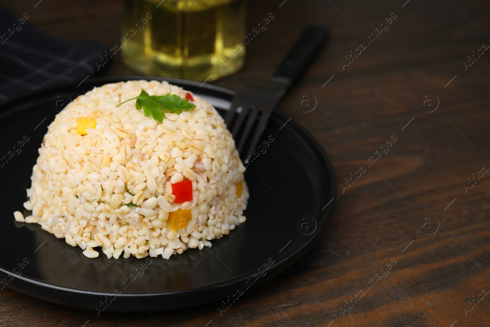 Photo of Delicious bulgur with vegetables and parsley served on wooden table, closeup. Space for text