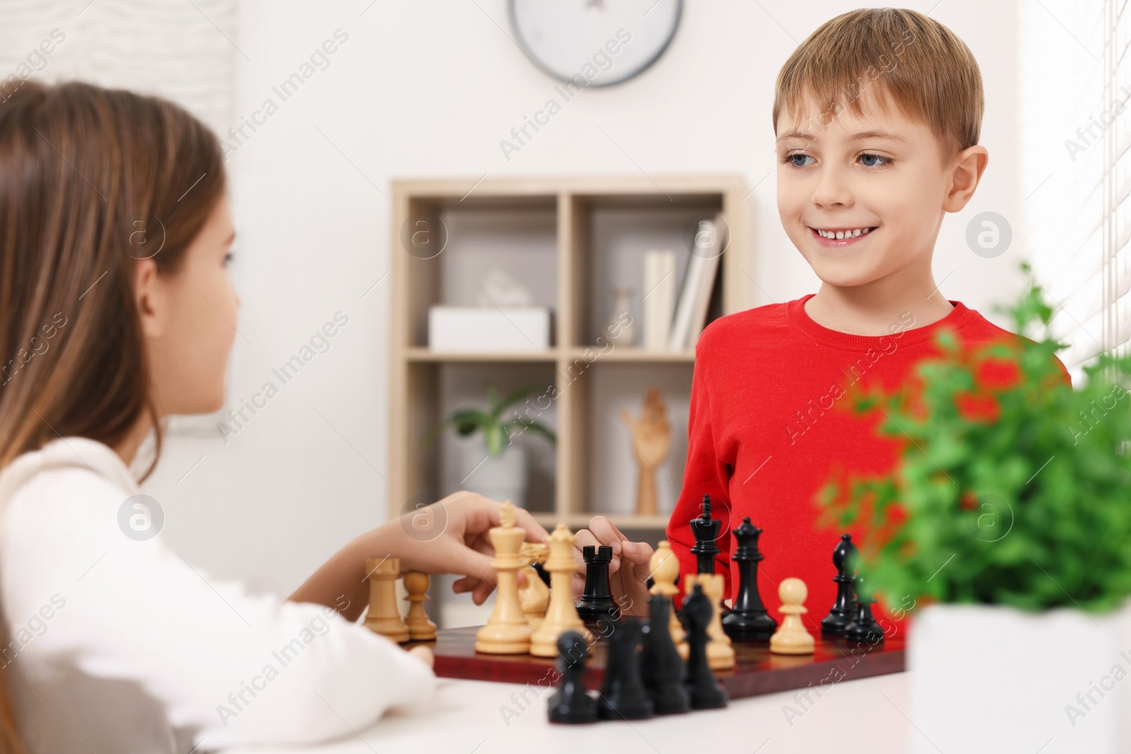 Photo of Cute children playing chess at table in room