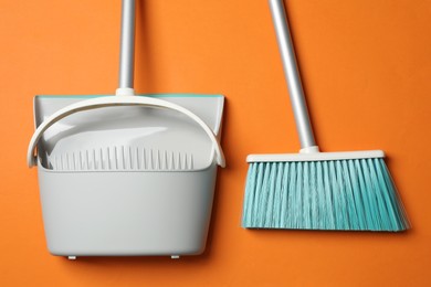Photo of Plastic broom and dustpan on orange background, flat lay