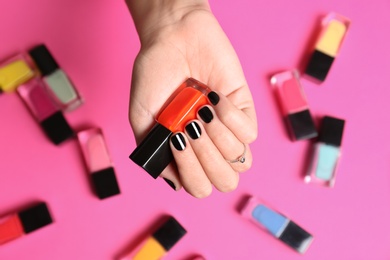 Photo of Woman with black manicure holding nail polish bottle on color background, top view