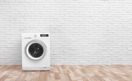 Photo of Modern washing machine near brick wall in empty laundry room, space for text