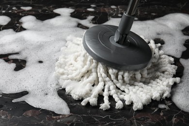 Photo of Cleaning black marble floor with string mop, closeup