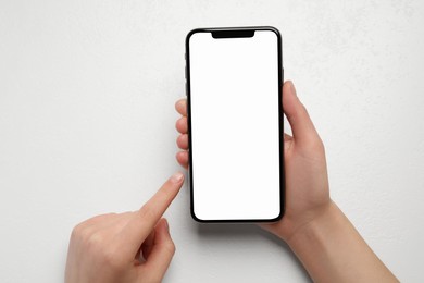 Woman holding smartphone with blank screen at white table, top view. Mockup for design