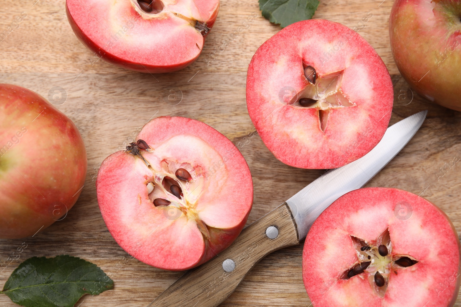 Photo of Tasty apples with red pulp, leaves and knife on wooden board, flat lay