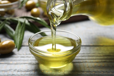 Photo of Pouring olive oil into bowl on wooden table, closeup. Healthy cooking