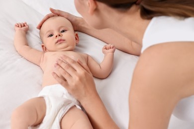 Photo of Woman applying body cream onto baby`s skin on bed, closeup