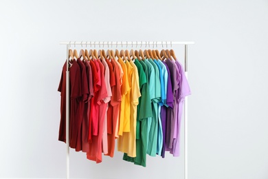 Photo of Rack with rainbow clothes on light background