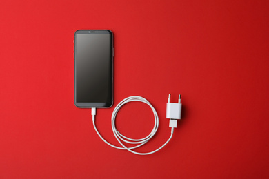 Photo of Smartphone and USB charger on red background, flat lay. Modern technology