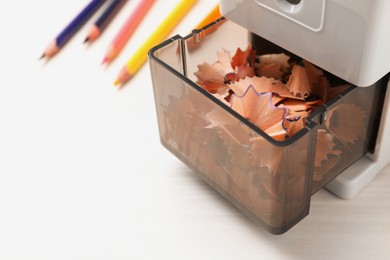 Mechanical sharpener with shavings near colorful pencils on white wooden table. Space for text