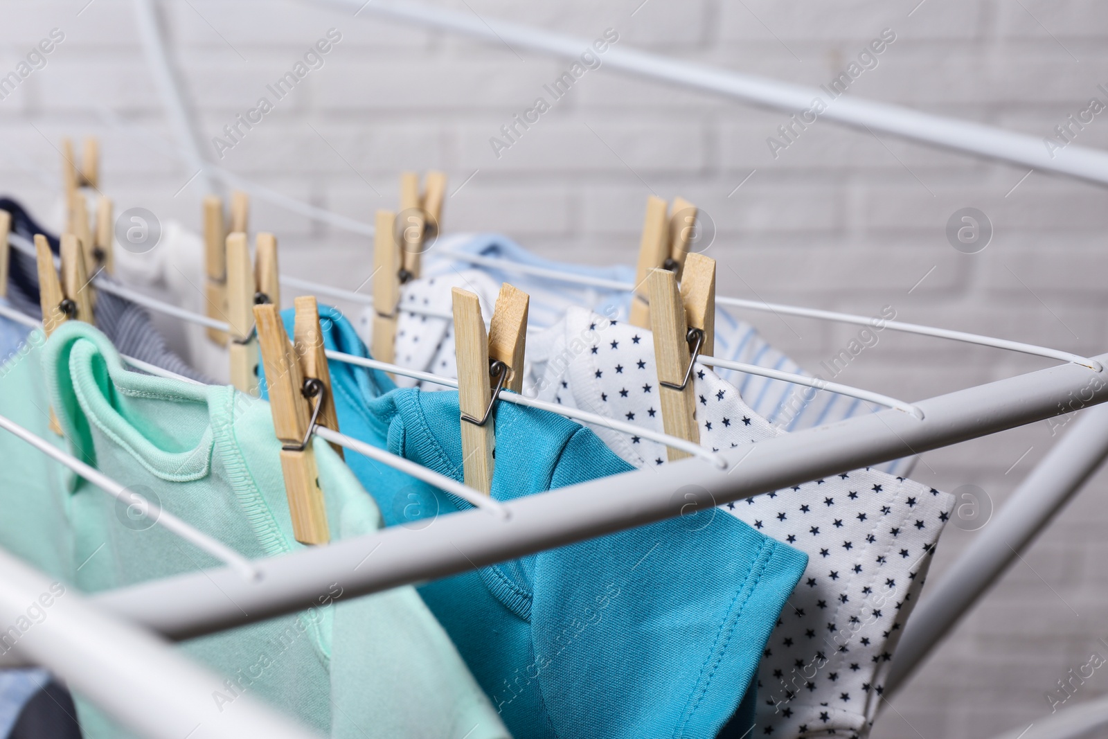 Photo of Different cute baby onesies hanging on clothes line near brick wall, closeup. Laundry day