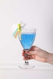 Photo of Woman holding glass of cocktail decorated with cotton candy and sour rainbow belt on white background, closeup
