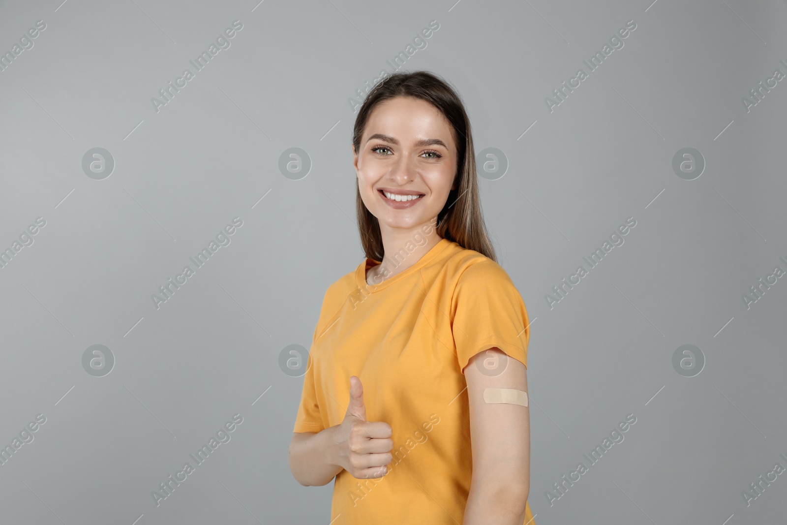 Photo of Vaccinated woman with medical plaster on her arm showing thumb up against grey background