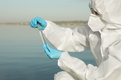 Photo of Scientist in chemical protective suit with test tube taking sample from river for analysis