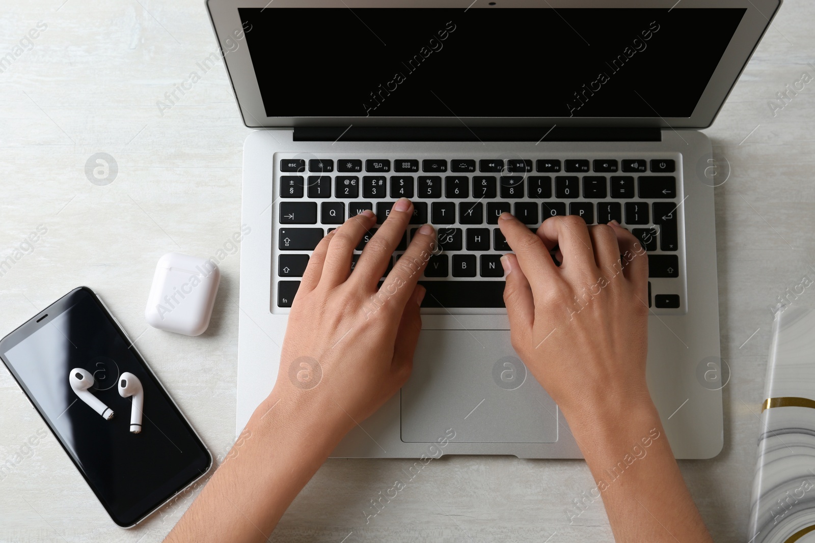 Photo of Woman with laptop, wireless earphones and mobile phone at light table, top view