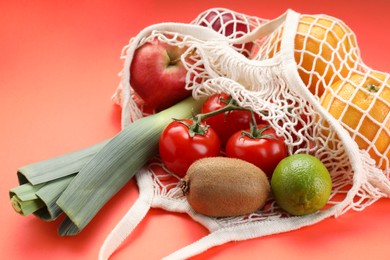 Photo of String bag with different vegetables and fruits on red background