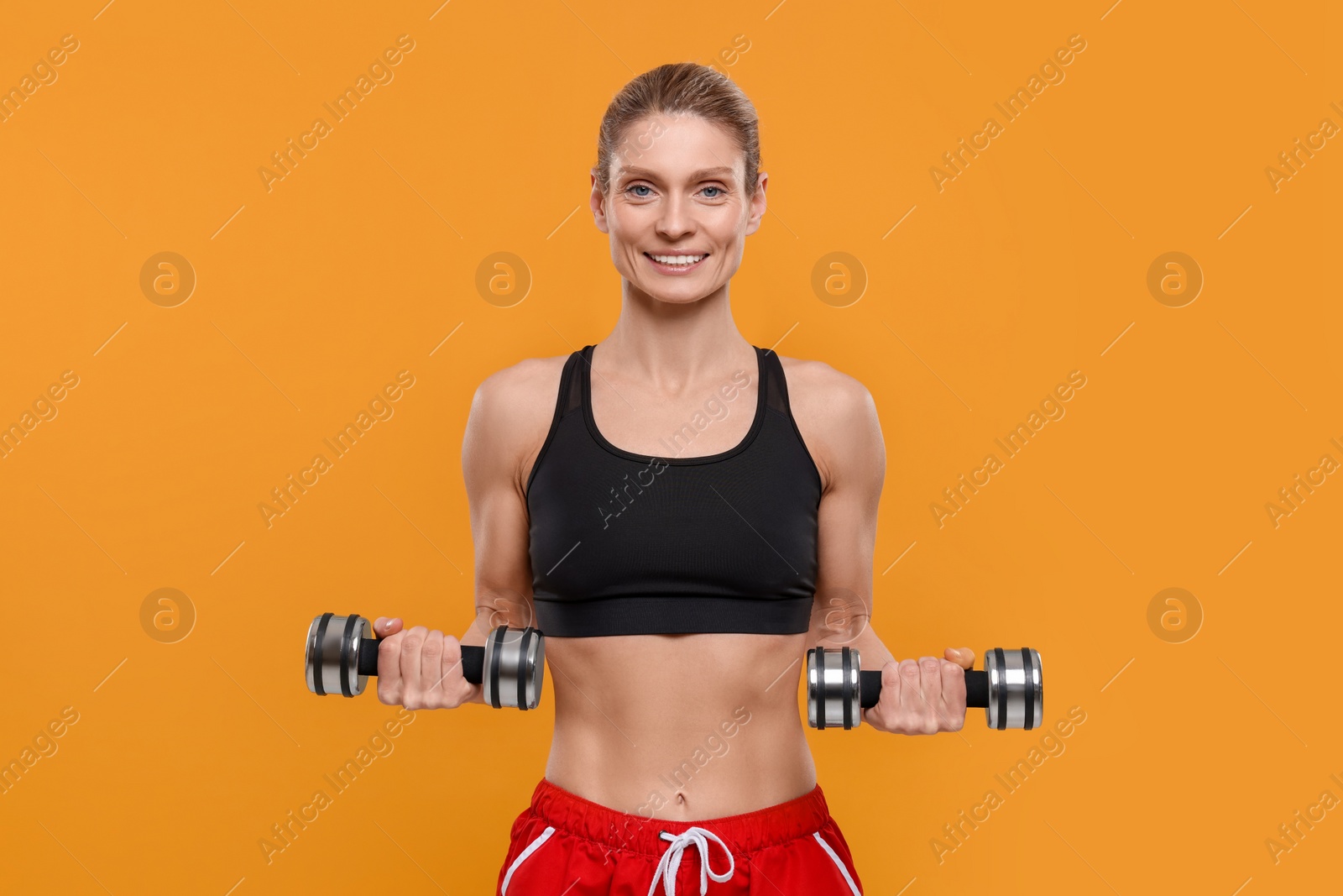 Photo of Portrait of sportswoman exercising with dumbbells on yellow background