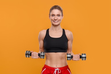 Portrait of sportswoman exercising with dumbbells on yellow background
