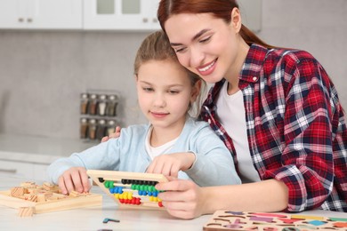 Photo of Happy mother and daughter playing with different math game kits at white marble table in kitchen. Study mathematics with pleasure