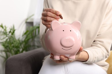 Photo of Woman putting coin into piggy bank at home, closeup