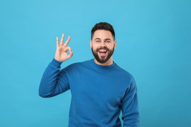 Photo of Happy young man with mustache showing OK gesture on light blue background