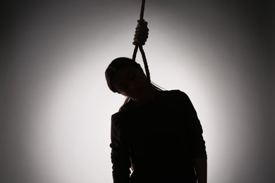 Silhouette of woman with rope noose on neck against light background