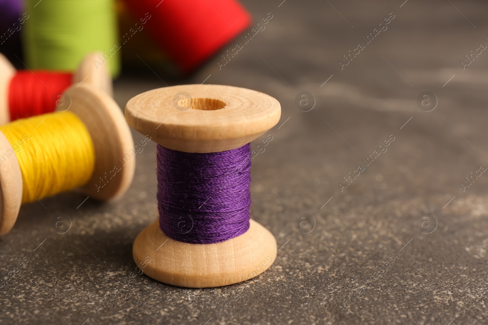 Photo of Set of color sewing threads on grey table, closeup. Space for text