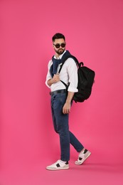 Young man with stylish backpack walking on pink background