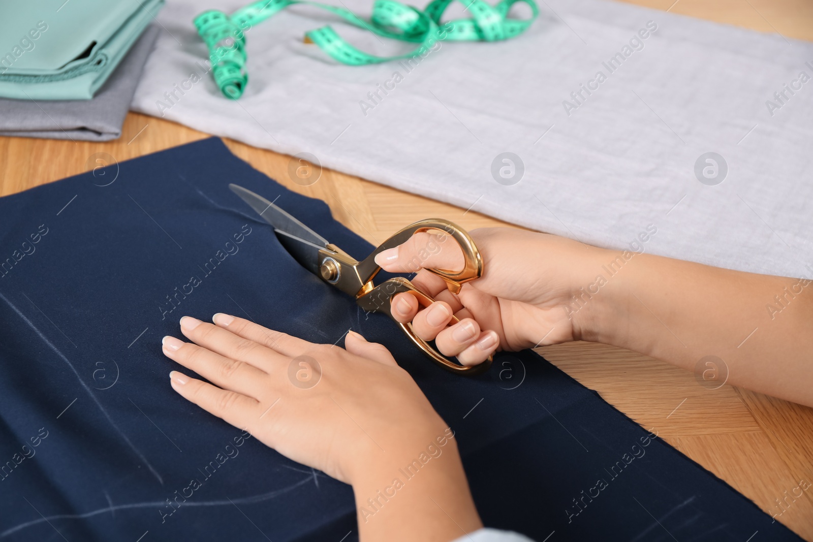 Photo of Woman cutting blue fabric with scissors at wooden table, closeup