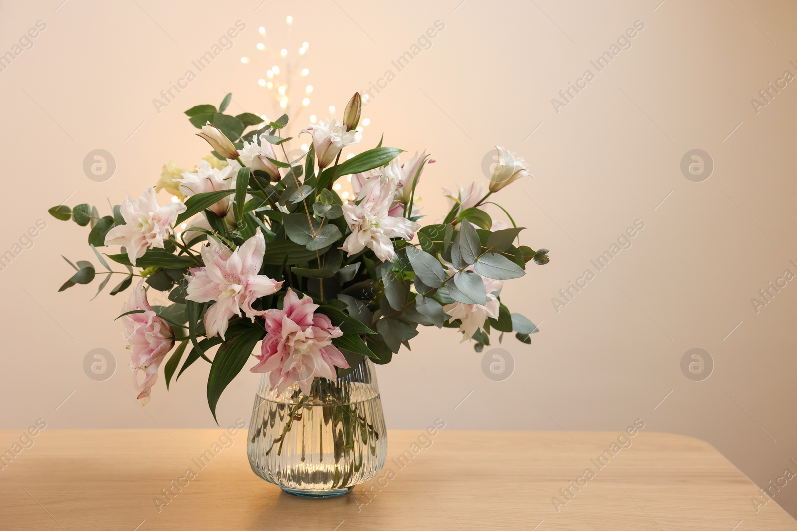 Photo of Bouquet of beautiful lily flowers in vase on wooden table against beige background, space for text