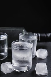 Photo of Bottle of vodka and shot glasses with ice on table against black background