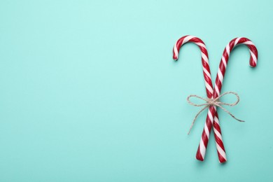 Photo of Two sweet Christmas candy canes with bow on turquoise background, top view. Space for text